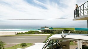 A white car parked on a street with a view of the ocean and a person on a balcony.