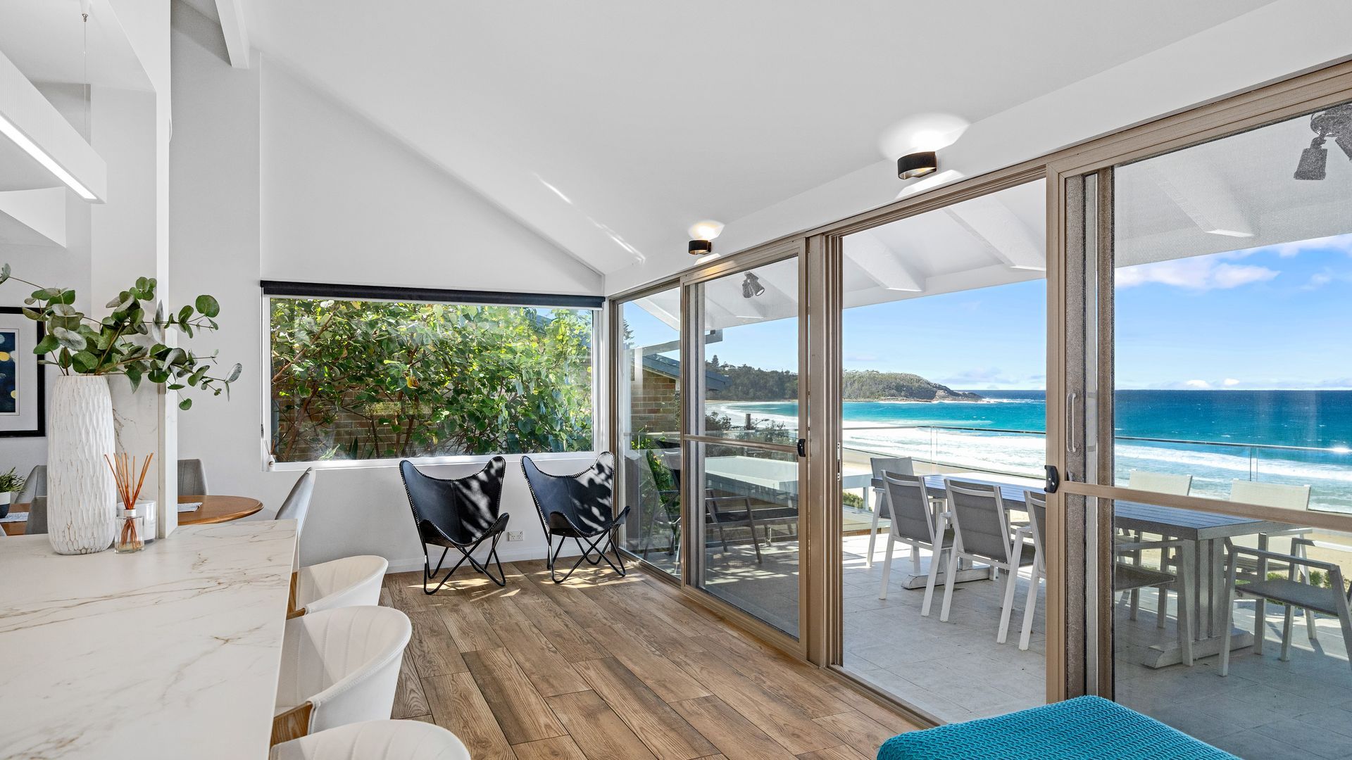 A modern interior with a large sliding glass door leading to a balcony overlooking a beach.