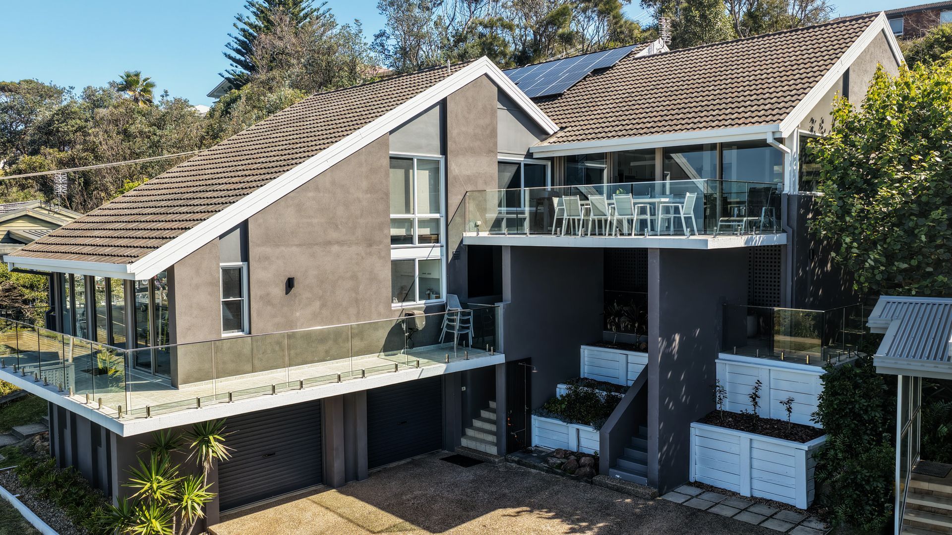 Een modern huis met twee verdiepingen, een plat dak, grote ramen en een balkon met tuinmeubilair.