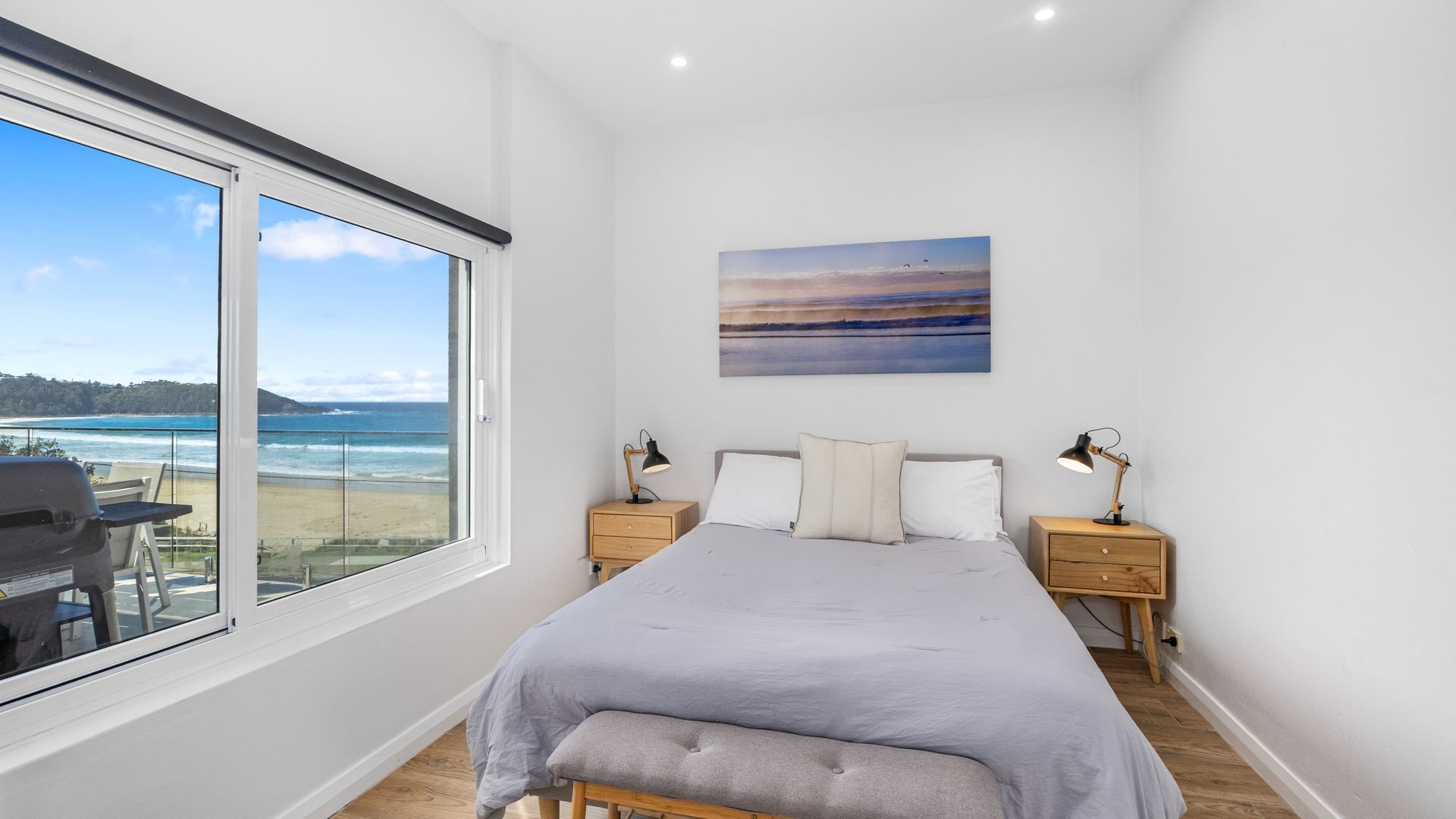 A bedroom with a large window, a bed, two bedside tables, and a painting on the wall.