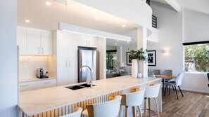 Une cuisine moderne dotée d’un plan de travail en marbre, d’appareils électroménagers en acier inoxydable et d’un coin bar avec des tabourets blancs.
