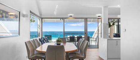 A dining area with a view of the ocean, a round table, and chairs.