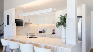 Une cuisine moderne avec des meubles blancs, un plan de travail en marbre et un îlot central doté de tabourets de bar.