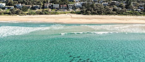 A coastal residential area with houses, clear turquoise waters, and a sandy beach.