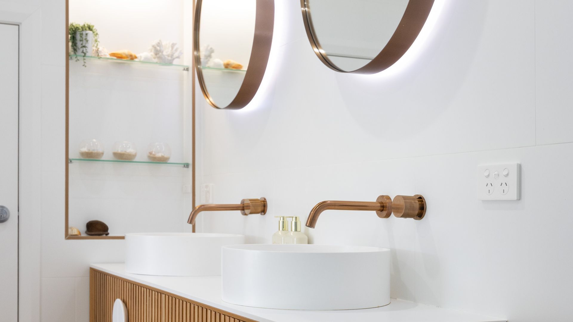 A bathroom with two sinks, a mirror, and a shelf with decorative items.