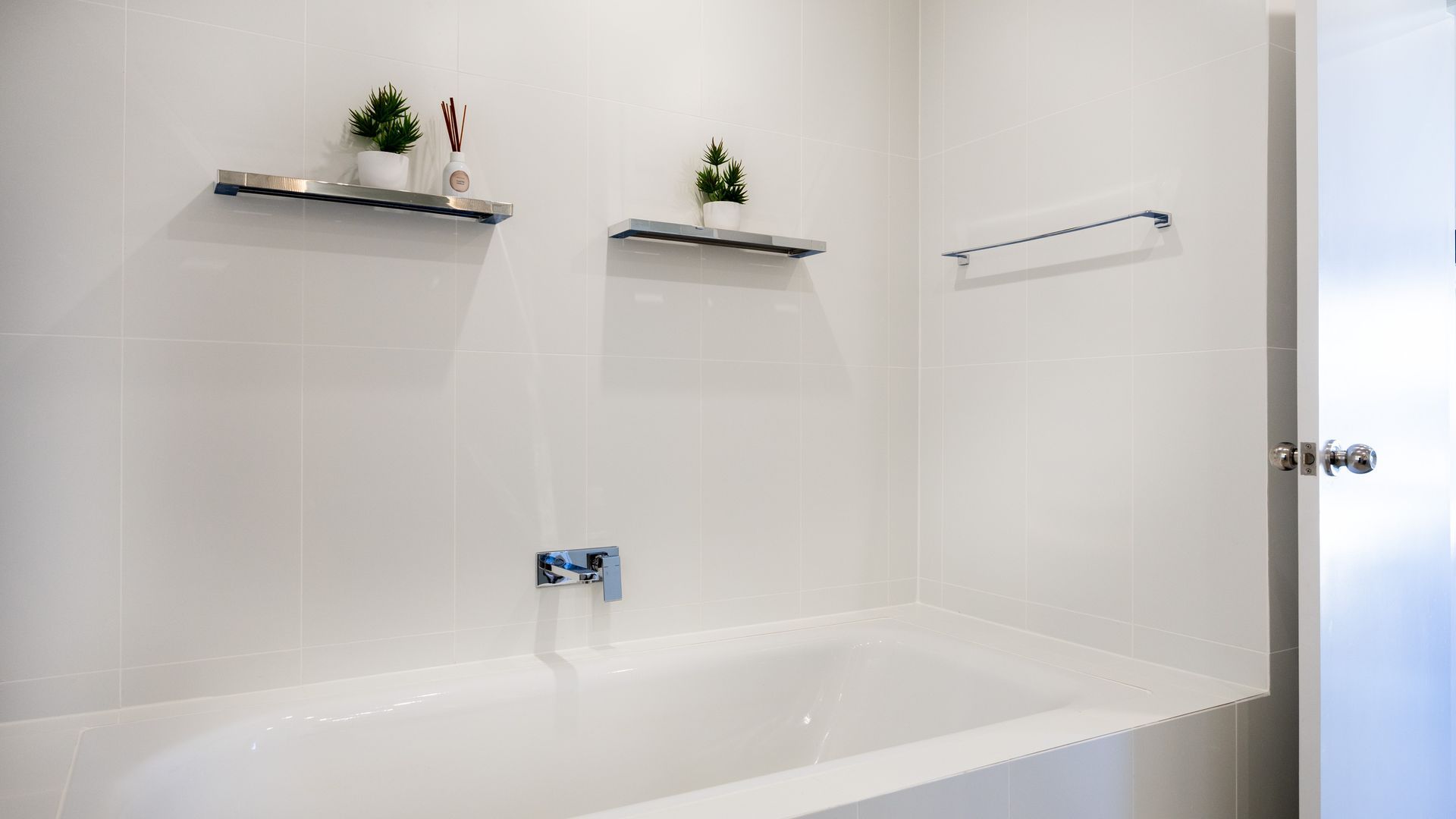 A modern bathroom with a white bathtub, two shelves with plants and a bottle, and a towel rack.