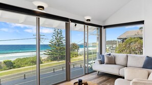 A modern living room with a large glass door leading to a balcony overlooking a coastal view.