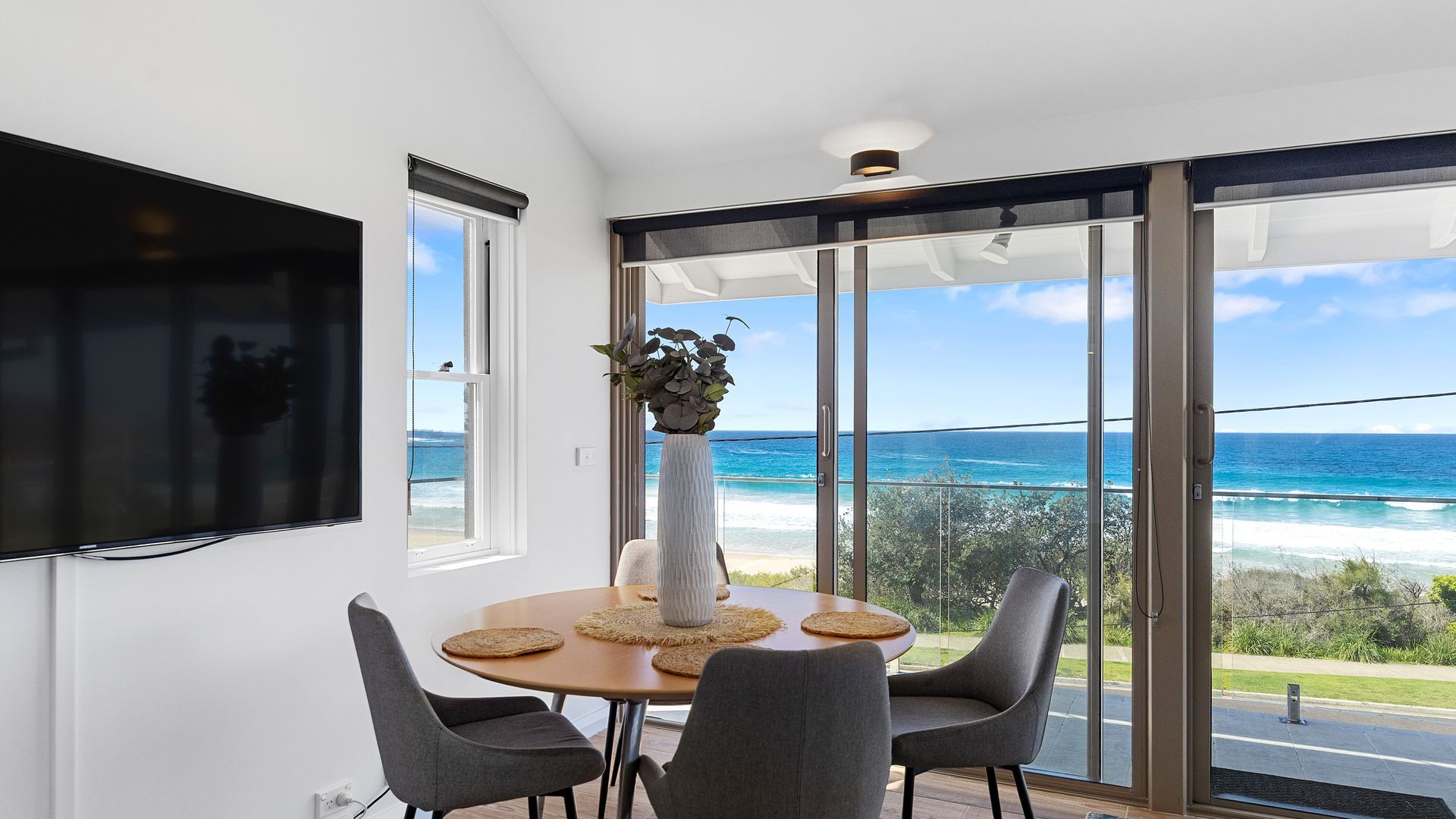 Un'area pranzo con tavolo e sedie, un'ampia finestra vista mare e un elemento decorativo con piante.