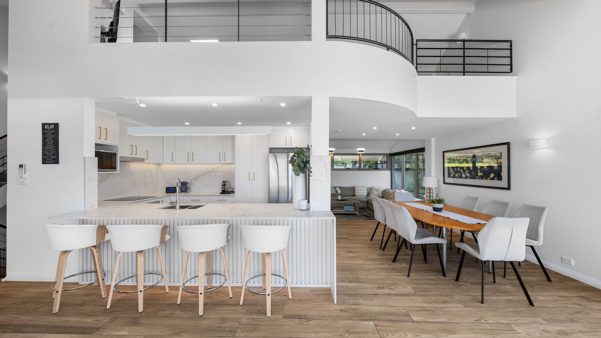Een moderne keuken met een centraal eiland, barstoelen en een eethoek met een houten tafel en stoelen.