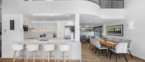 Een moderne keuken met een centraal eiland, barstoelen en een eethoek met een houten tafel en stoelen.