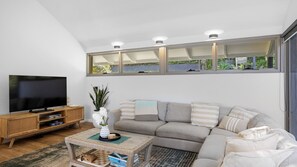 A modern living room with a television, sofa, and a large window with a view of greenery.