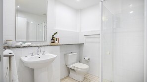 A modern bathroom with a white sink, toilet, and glass shower enclosure. - Surfers Reef Escape in Mollymook (Mollymook Beach)