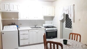 A compact kitchen with white cabinets, a stove, a sink, and a table with chairs.