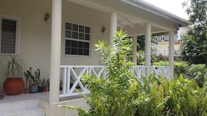 A covered porch with white railings, potted plants, and a window with a grid pattern.
