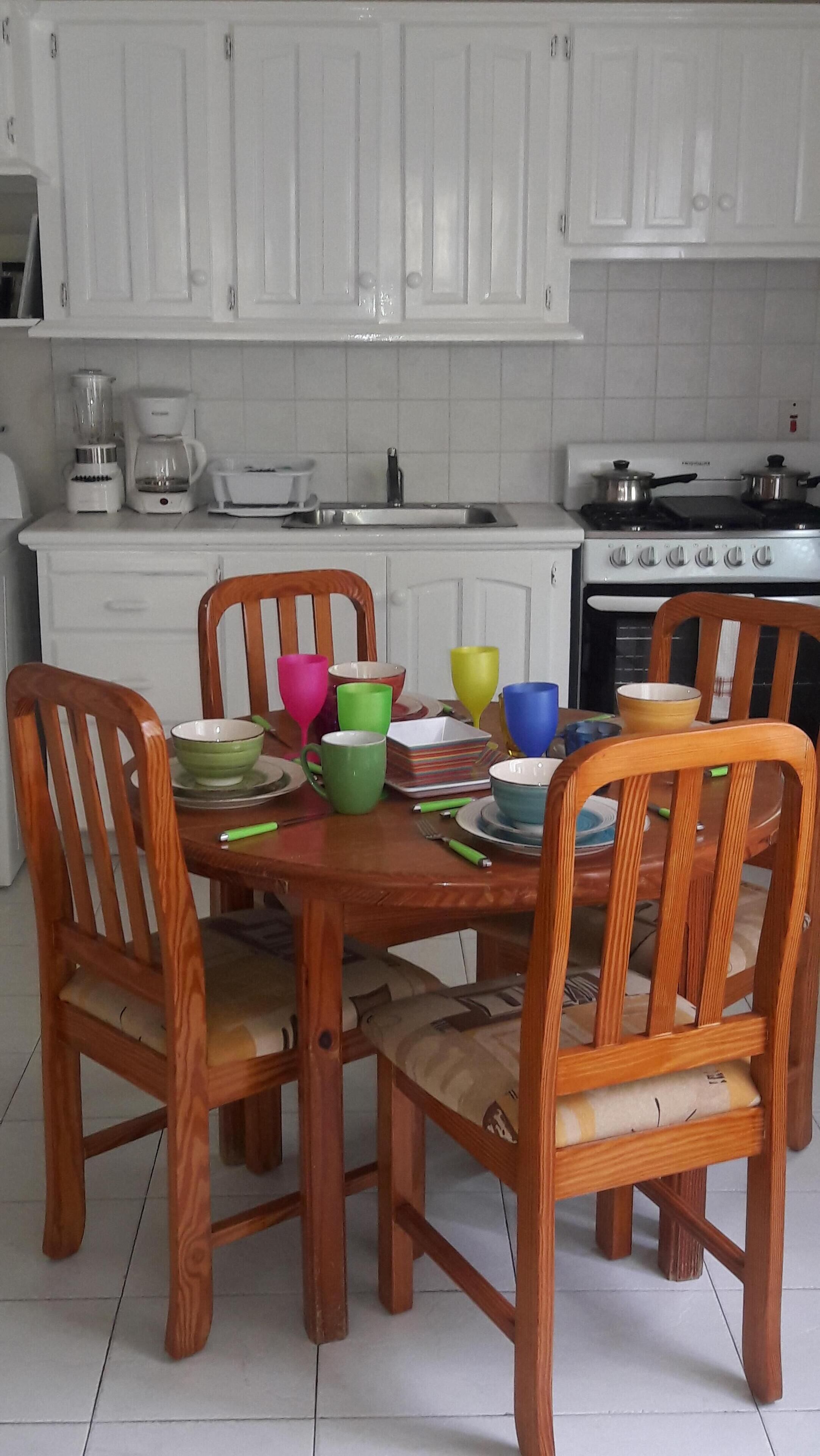 A wooden dining table with chairs, surrounded by colorful bowls and plates.