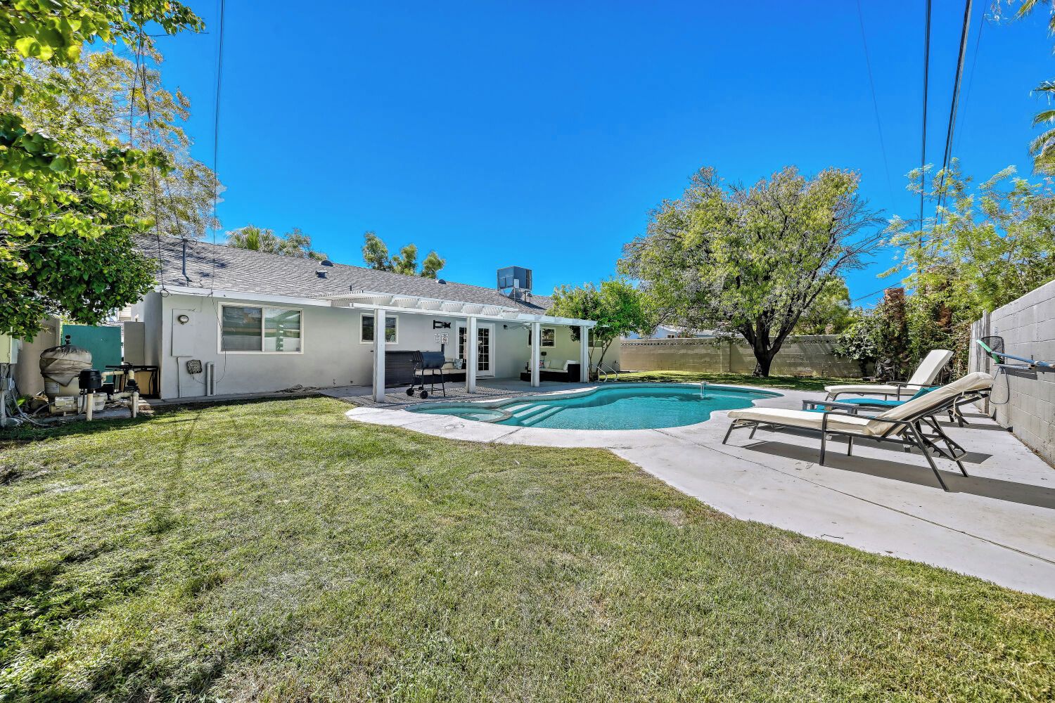 A residential backyard with a swimming pool, a covered patio, and a lawn.