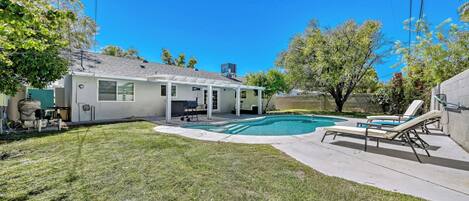 A residential backyard with a swimming pool, a covered patio, and a lawn.