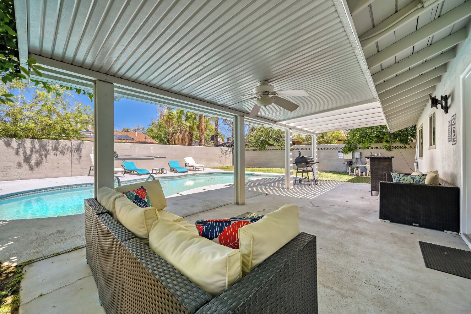 A covered outdoor area with a pool, lounge chairs, and a barbecue grill.