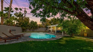 A backyard with a swimming pool, a covered patio, and a lawn with lounge chairs.