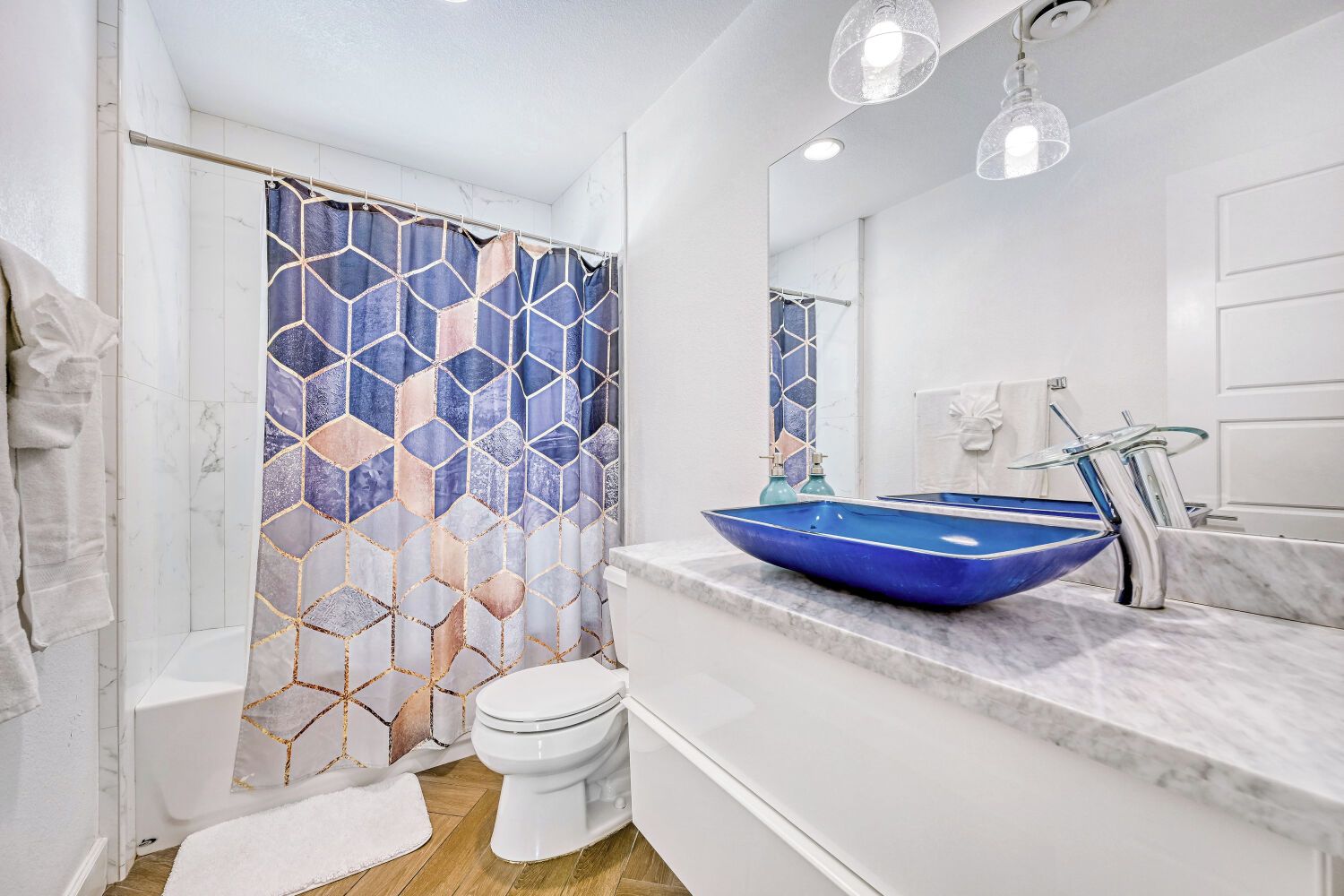 A bathroom with a white toilet, a blue vessel sink, a shower curtain with a geometric pattern, and a marble countertop.