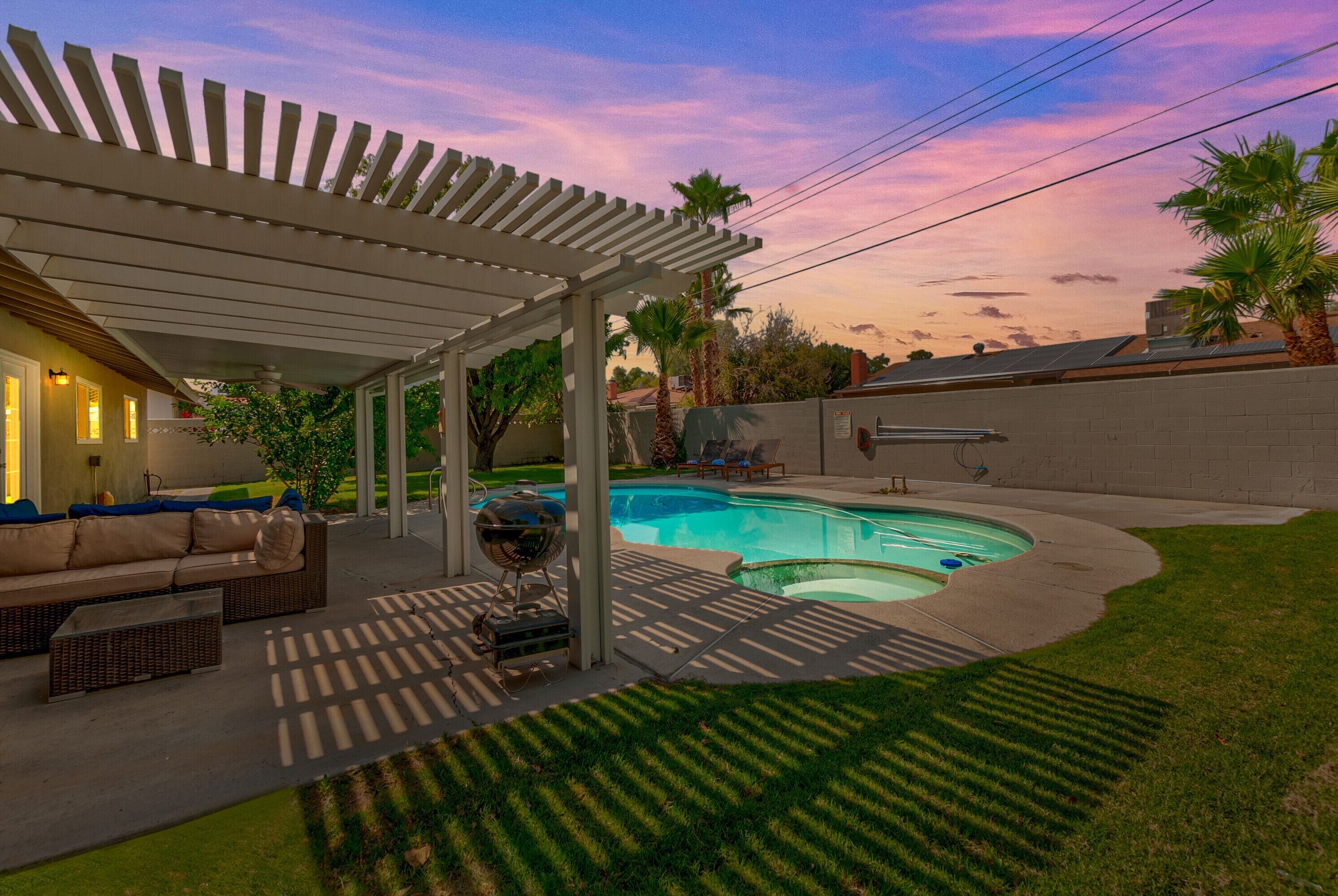 A backyard with a swimming pool, covered patio, and outdoor furniture.