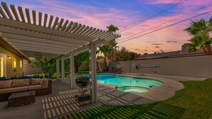 Un jardin avec une piscine, un patio couvert et du mobilier d’extérieur.