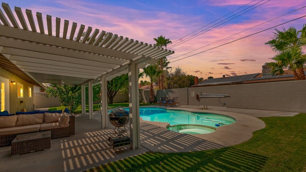 A backyard with a swimming pool, covered patio, and outdoor furniture.
