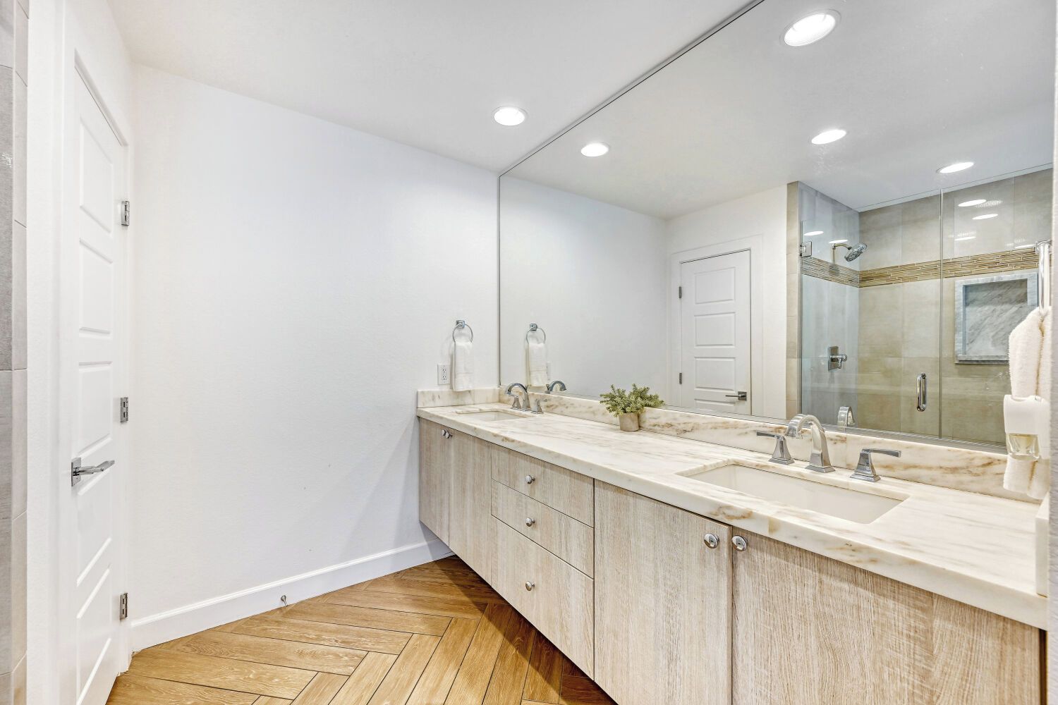 A modern bathroom with a large mirror, two sinks, and a shower area.