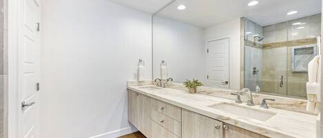 A modern bathroom with a large mirror, two sinks, and a shower area.