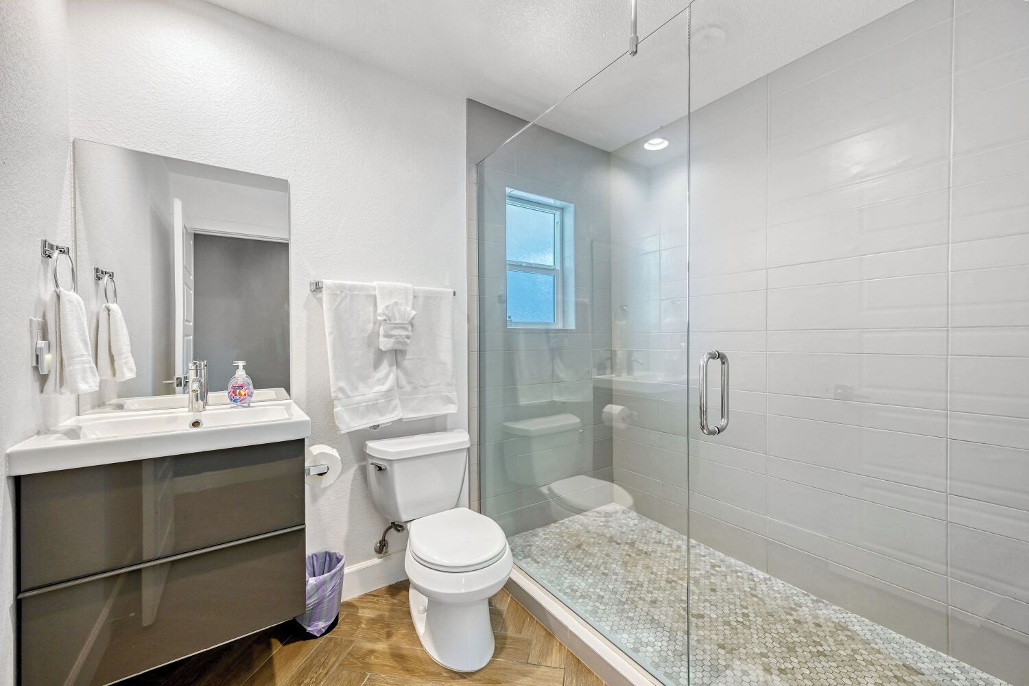 A modern bathroom with a glass-enclosed shower, a toilet, and a sink with a mirror above it.