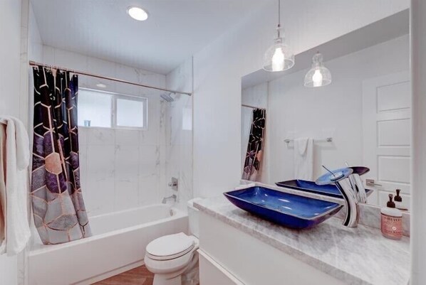 A modern bathroom with a bathtub, toilet, and a sink with a blue basin.