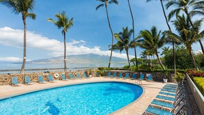 A pool with lounge chairs and palm trees, overlooking a body of water and mountains.