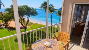 A balcony with a round glass table and wooden chairs, overlooking a beach and ocean.