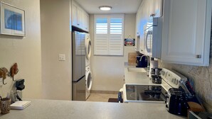 Cozinha compacta com armários brancos, máquina de lavar e secar embutidas, fogão e cafeteira.