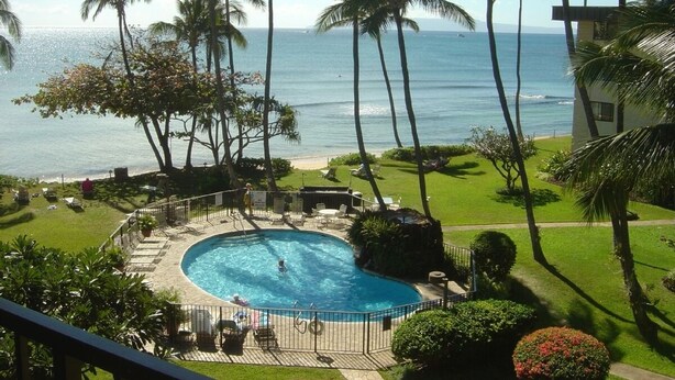 Piscina com vista para o oceano, rodeada por palmeiras e um edifício.
