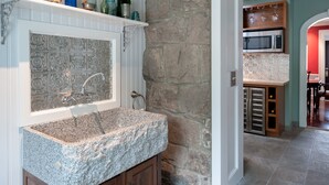 A kitchen with a granite countertop, a stainless steel sink, and a stone backsplash. - A Historic Place to Stay for Your Historic Days. Gracious Granite Home + Tavern (Waterford)