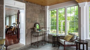 A room with a stone wall, large windows, a fireplace, and a seating area with a table. - A Historic Place to Stay for Your Historic Days. Gracious Granite Home + Tavern (Waterford)