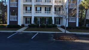 A multi-story building with a symmetrical facade, balconies, and a parking lot in front.