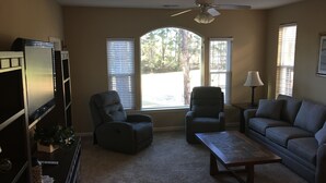 A living room with a TV, two armchairs, a sofa, a coffee table, and a ceiling fan.