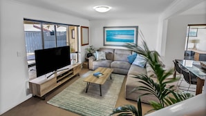 A living room with a flat-screen TV, a sofa, a coffee table, and a dining area with a glass table and chairs. - Luxury Spa “Beachfront Moana”
Perfect for couples, families or friends! (Moana)
