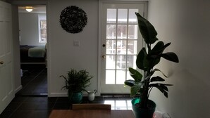 A hallway with a door leading to a bedroom, a potted plant, and a decorative wall piece. - Elegant NYC Pad with Wifi (Queens)