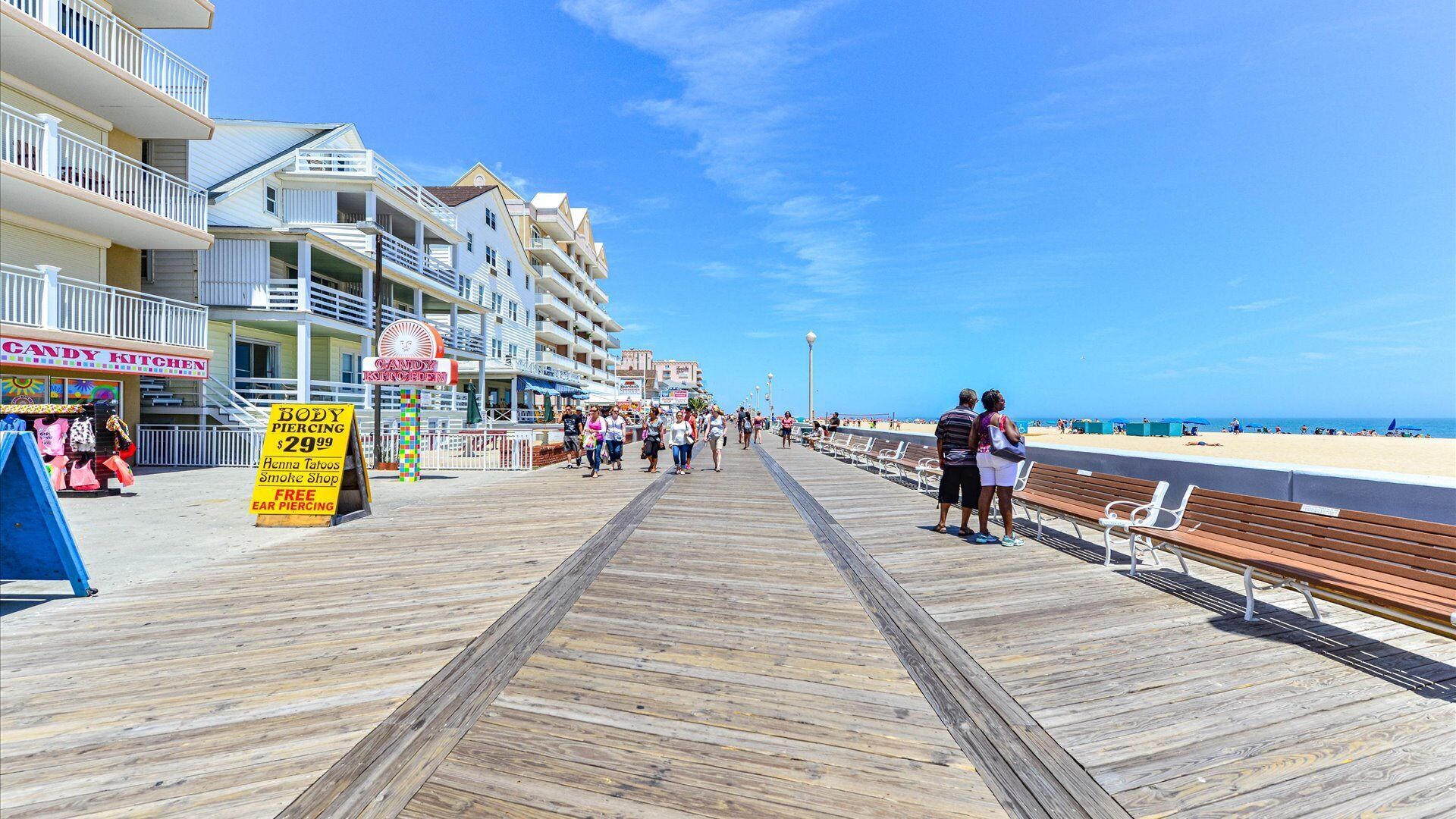 A wooden boardwalk leading to a beach with a candy shop and piercing services.