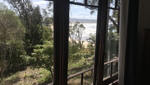 Et værelse med stort vindue der udover en strand og skov.