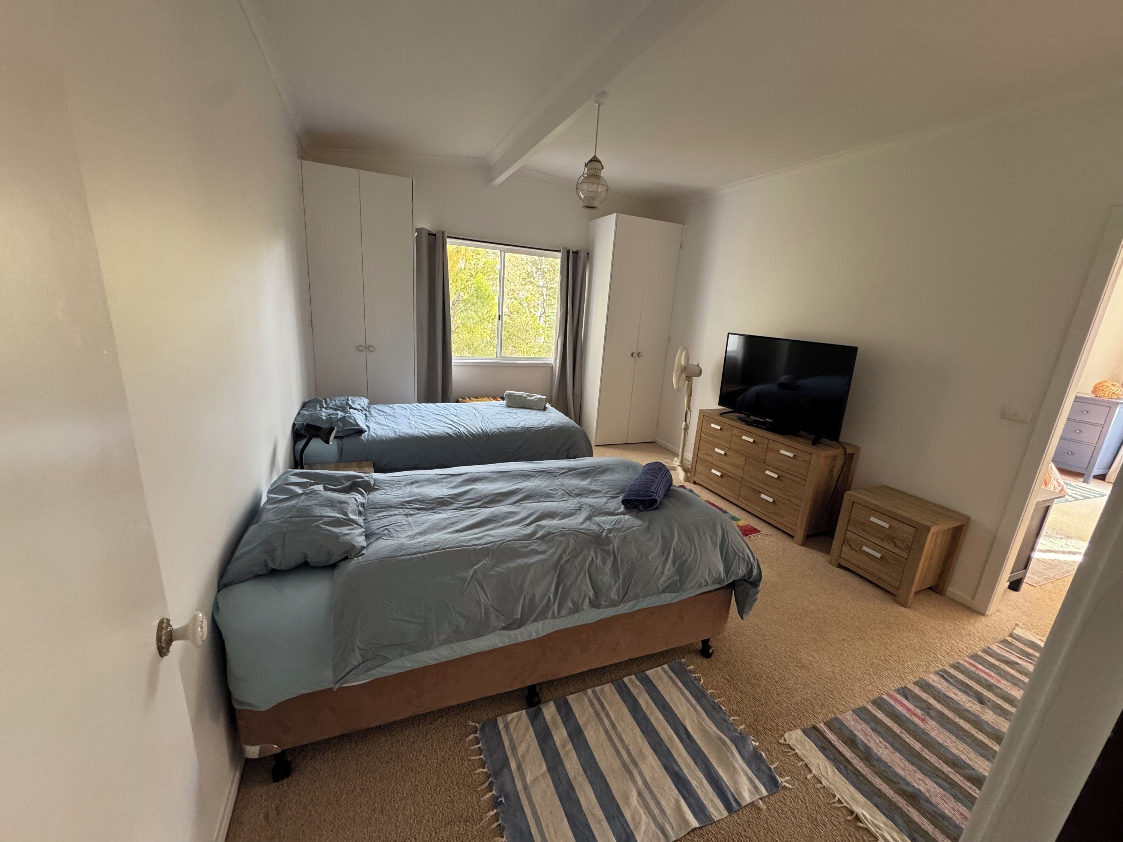 Een slaapkamer met twee bedden, een televisie, een dressoir en een raam.