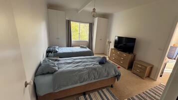 Een slaapkamer met twee bedden, een televisie, een dressoir en een raam.