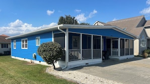 Uma casa azul com varanda coberta e uma pequena árvore na frente.