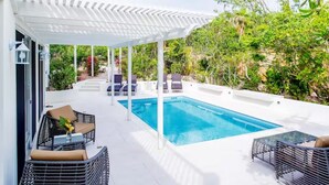 A poolside area with a white pergola, wicker furniture, and a clear blue pool.