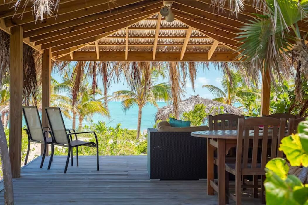 Un espacio de estar al aire libre cubierto con vistas al océano, muebles de madera y una estructura de techo de paja.