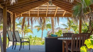 A covered outdoor seating area with a view of the ocean, wooden furniture, and a thatched roof structure.