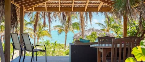 Un espacio de estar al aire libre cubierto con vistas al océano, muebles de madera y una estructura de techo de paja.
